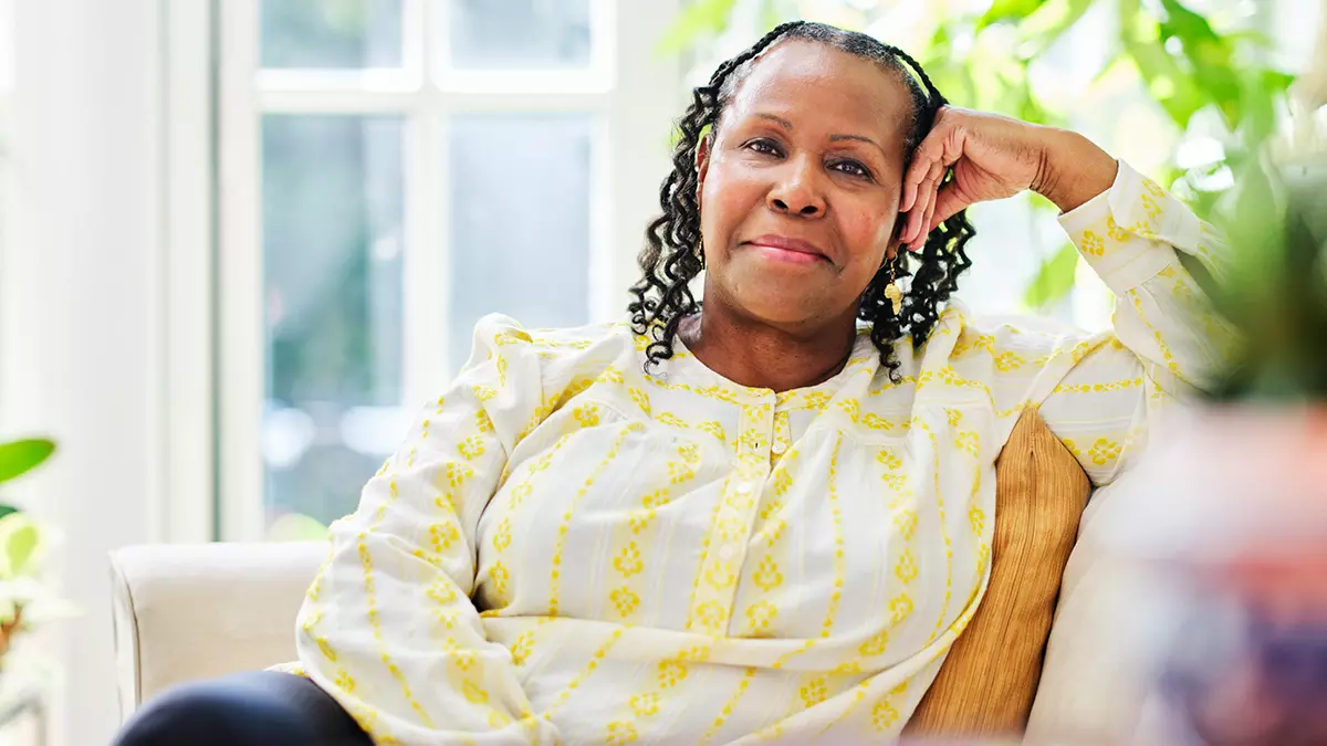MSK patient Linda Collins in a yellow-patterned blouse sits in a bright room, resting her head on her hand and smiling softly.