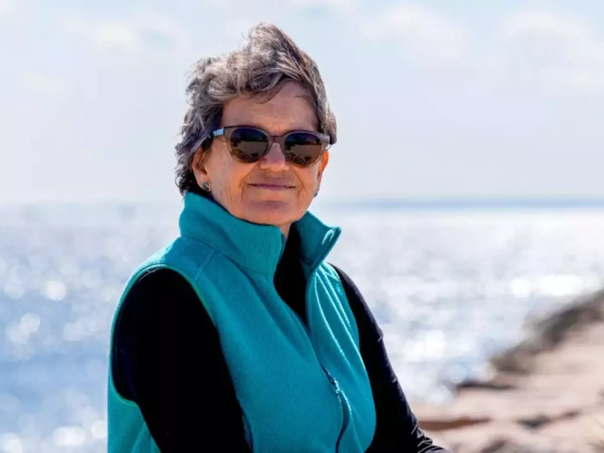 MSK patient Joanna wearing sunglasses and a teal vest, smiles while standing near a sunlit waterfront.