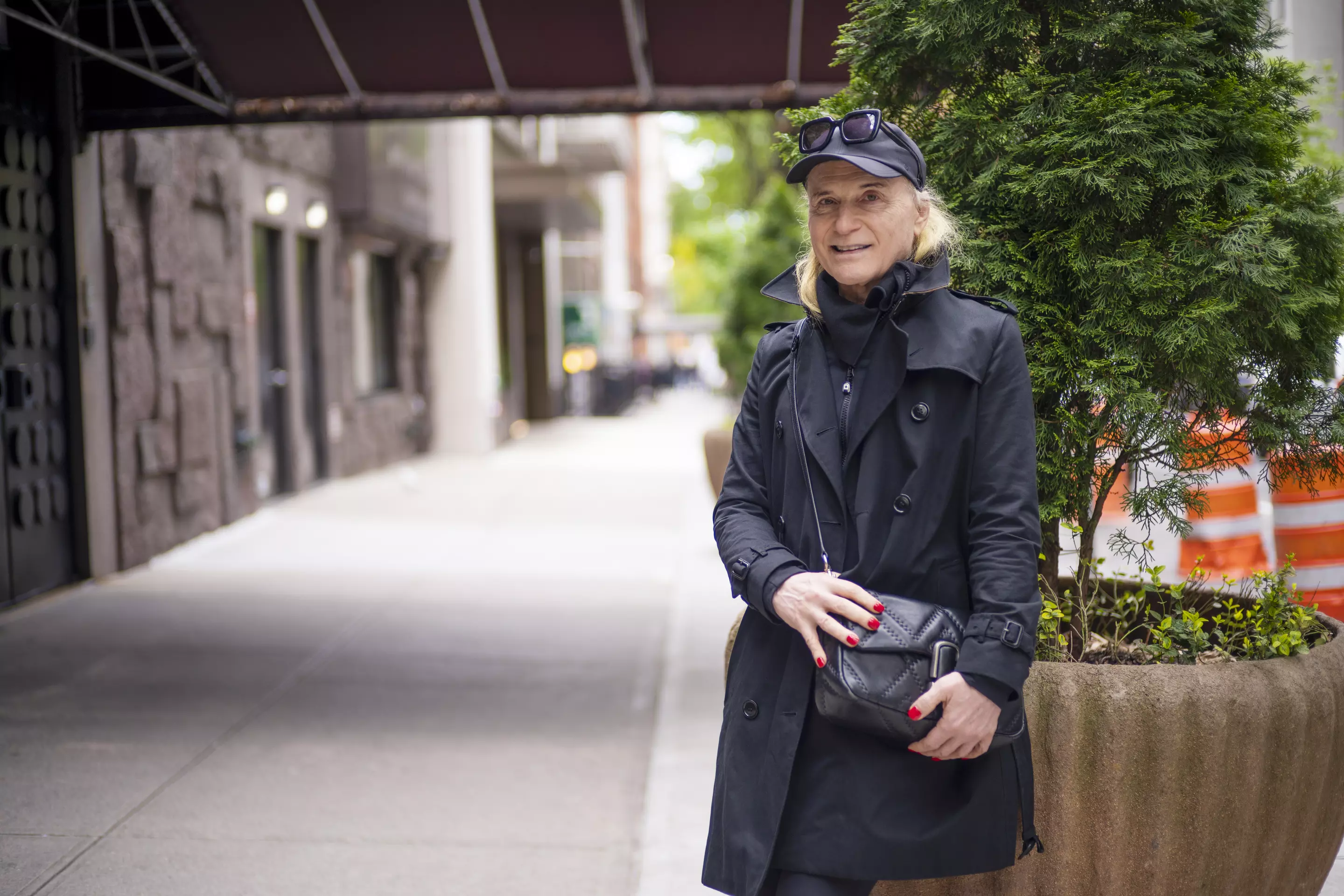 MSK patient Susan dressed in black with a hat and sunglasses on their head stands on a city sidewalk, smiling.